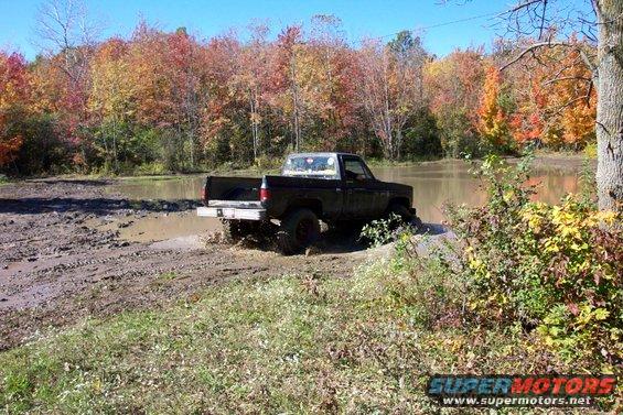 Black pickup truck navigating a muddy trail with fall foliage in the background