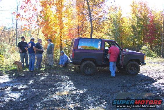 Purple and black Ford Bronco with off-road tires stuck in mud, people standing around