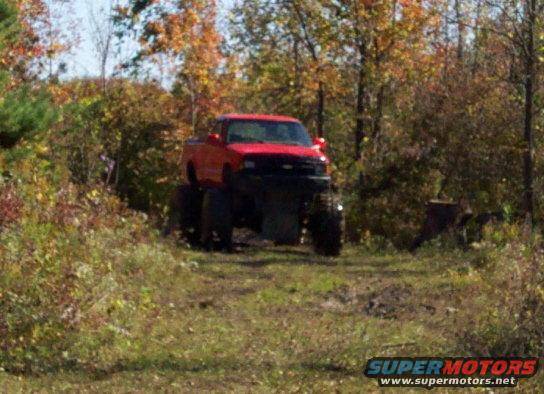 Red lifted pickup truck with large tires on a dirt path