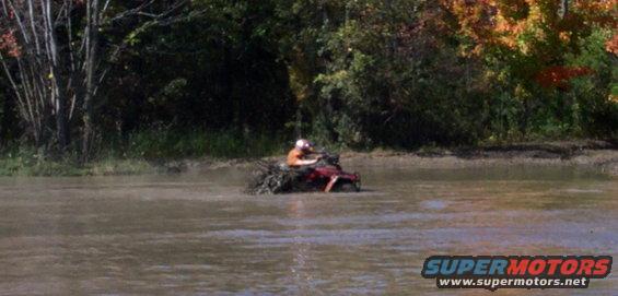 Red ATV stuck in muddy water with trees in background