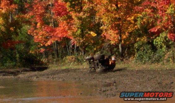 ATV overturned in mud with fall foliage in background