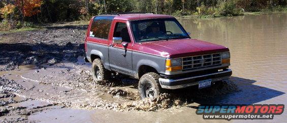 Red 1978 Ford Bronco with a black grille and white wheels parked on a dirt surface