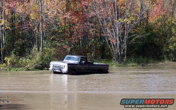 White pickup truck driving through floodwaters with trees in background