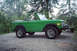 1975 Ford Bronco - A green 1975 Ford Bronco is parked outdoors with a bicycle rack attached to its front bumper.