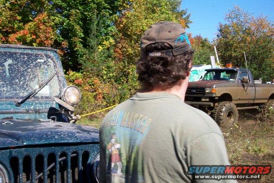 Muddy Jeep and Ford truck in a field with fall foliage