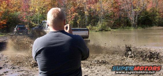 Two trucks driving through mud, kicking up water and dirt