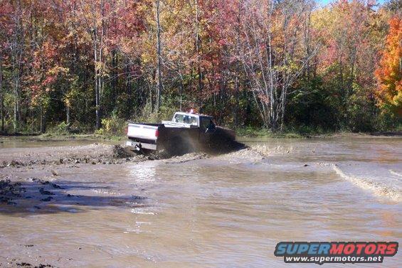 Truck driving through a muddy area with trees in the background