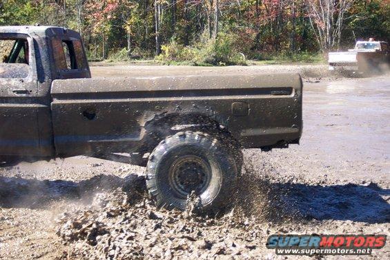 Mud-splattered dark brown Ford pickup truck driving through mud, side view