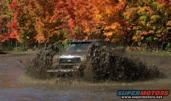 Truck splashing through mud with fall foliage in background