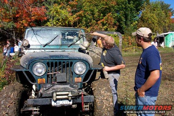 Two guys looking at a muddy Jeep Wrangler, another Jeep behind it