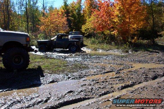 Off-road vehicles navigating a muddy track with autumn trees in the background