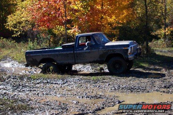 Dark pickup truck stuck in mud, side view, autumn trees in background