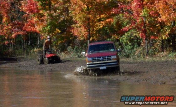 red van splashing through a muddy puddle with fall foliage in the background