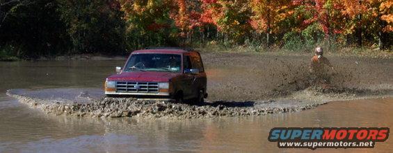 Red SUV driving through mud puddle, autumn trees in background