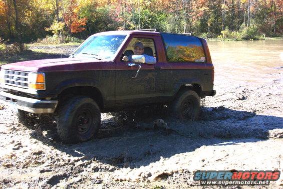 Maroon and black Ford Bronco stuck in mud with a person driving