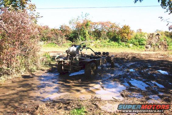 Off-road buggy with a large tank on the back stuck in mud, with four auxiliary lights on the front