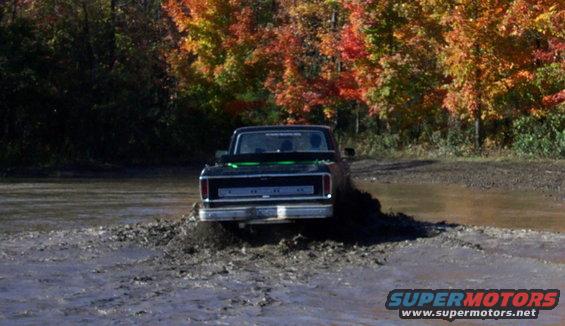 Black Ford pickup truck driving through mud with fall foliage in background