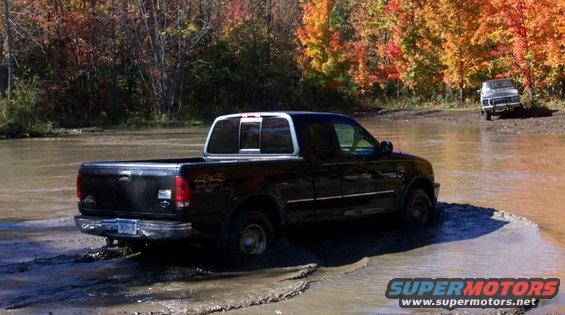Black pickup truck partially submerged in muddy water, with a second vehicle visible in the background