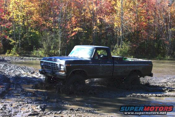 Dark blue pickup truck with a grille from the late 1970s driving through mud