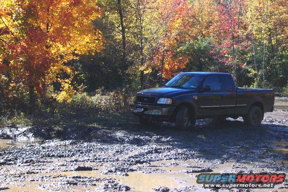 Black pickup truck stuck in mud with fall foliage in background