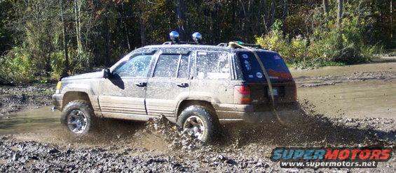 Muddy Jeep Grand Cherokee driving through a water-filled ditch