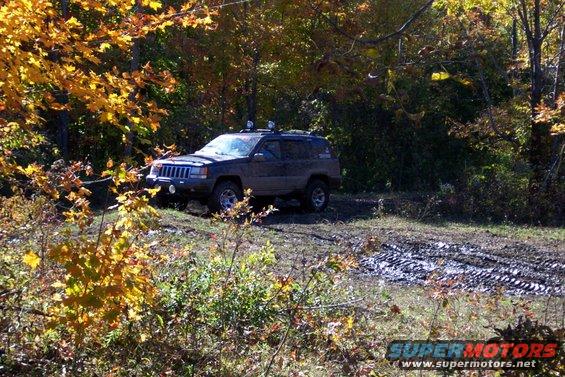 Dark colored Jeep Grand Cherokee driving on a muddy trail with fall foliage