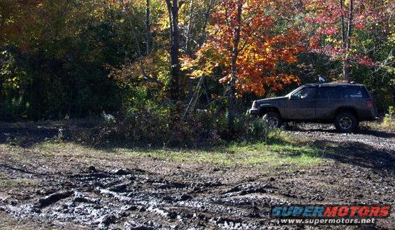 Dark colored Jeep Grand Cherokee parked on a muddy trail with fall foliage in the background