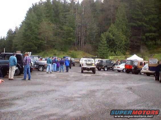 White pickup truck with front-end damage in a parking lot with other vehicles and people