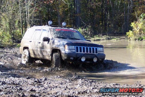 Muddy Jeep Grand Cherokee driving through water and mud on a wooded trail