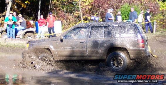 Mud-splattered dark SUV driving through a muddy puddle, side view