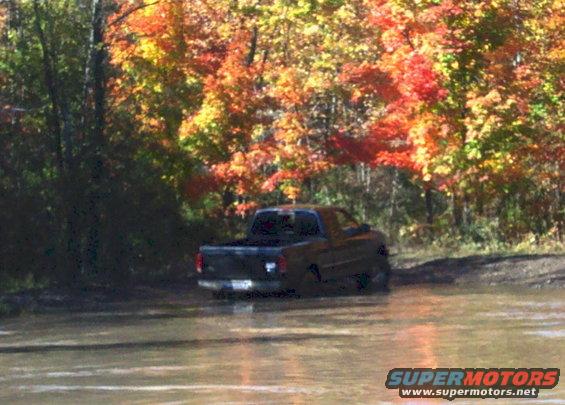 Black pickup truck driving through muddy water with fall foliage in the background