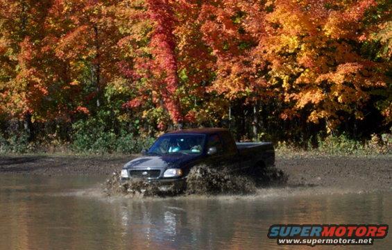 Black pickup truck with a grille from the late 1990s driving through mud and water