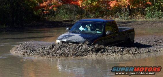 Black pickup truck stuck in deep mud and water, with fall foliage in the background