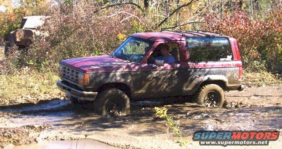 Red SUV stuck in mud, with another vehicle in the background