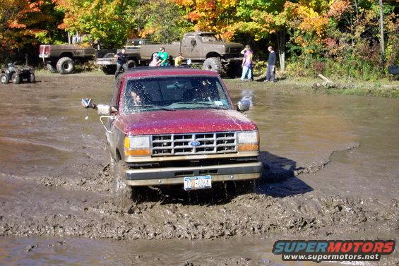 Red 1989 Ford Ranger pickup truck driving through mud. Front view