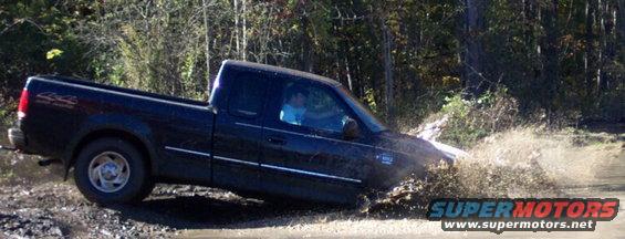 Black pickup truck splashing through mud on a dirt road