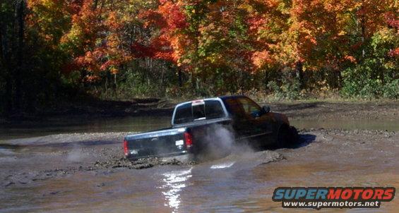 Black pickup truck driving through mud with fall foliage in background