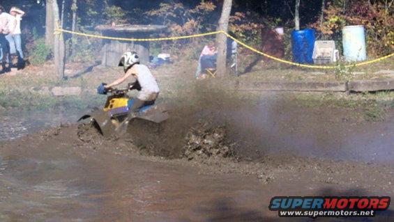 Yellow and blue ATV splashing through mud, rider wearing a helmet