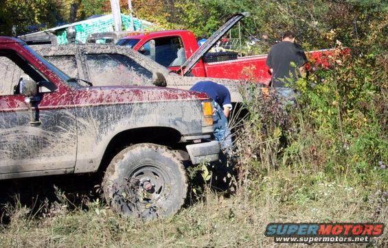 Mud-covered maroon SUV and red pickup truck in grassy area