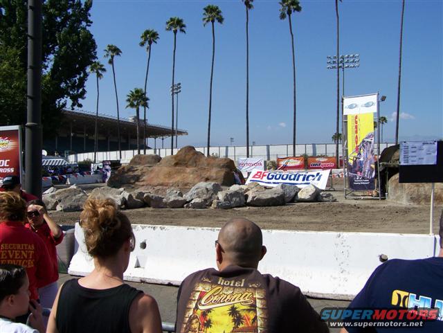 dirt track with rocks and palm trees, people watching event