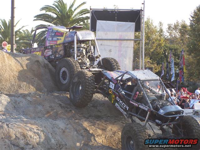 Two custom off-road buggies climbing a dirt hill, one behind the other
