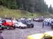 1976 Ford F-100 - Many off-road vehicles and people gathered in a parking area with a wooded hillside.