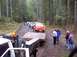 1976 Ford F-100 - A group of off-road vehicles are seen on a dirt road in a wooded area, with some people gathered near a trailer.