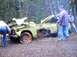 1976 Ford F-100 - A severely damaged pickup truck sits in a wooded area with people looking at it.