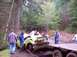 1976 Ford F-100 - A severely damaged sedan is being winched onto a trailer in a forest setting.