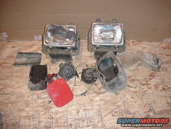 Two rectangular headlights, a red fuel cap, and two horns laid out on a wooden surface