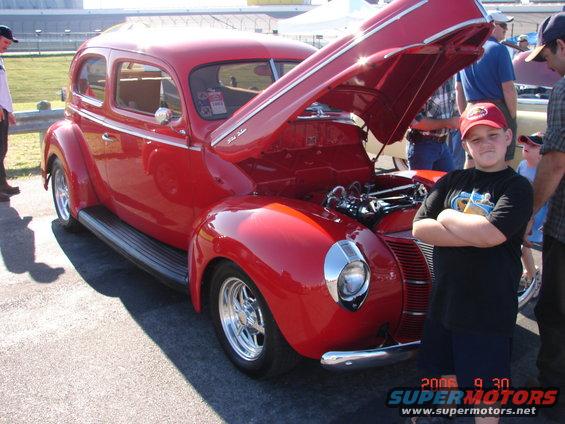 Red 1940 sedan with hood open, chrome accents, and custom wheels