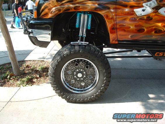 Lifted truck front wheel with custom spade and ace graphics, flame paint, and blue suspension components