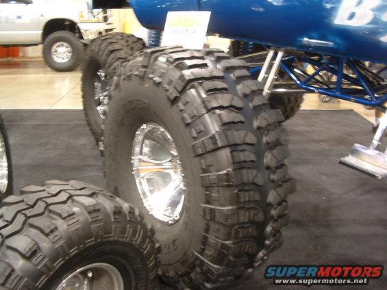 Oversized off-road tires and chrome rims on a custom vehicle; another truck visible in background