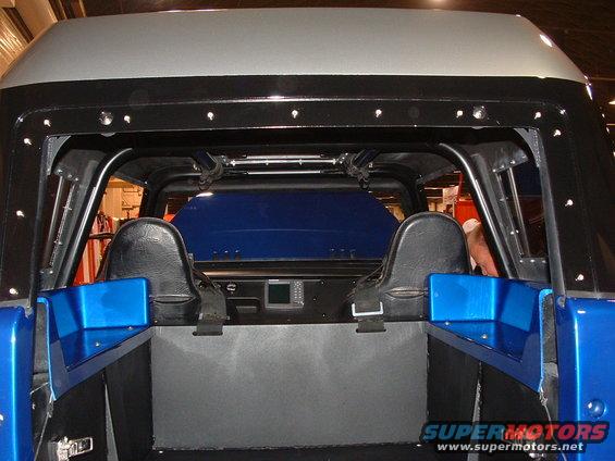 Back view of a custom pickup truck's interior, showing two bucket seats, a roll cage, and a blue bed cover
